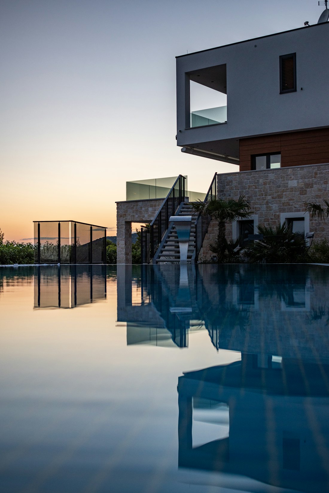 Modern waterfront home with clean glass balcony railings, reflected in still water at sunset